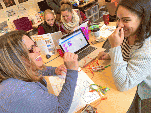 A group of teachers from New Bedford Public Schools interact with the MaKey MaKey and Scratch. They are connecting the MaKey MaKey alligator clips to brass fasteners on a map of the US and subsequently programming Scratch to trigger facts about each state or state capital.